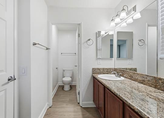 A bathroom with a granite counter top with a sink and large mirror.