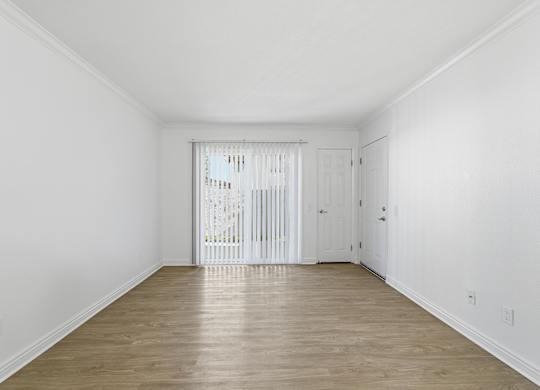 A spacious living room with wood floors and sliding glass door leading to a balcony/patio..