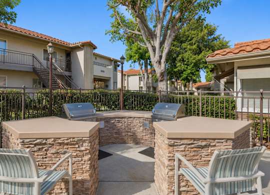 An outdoor grilling area with two grills and chairs.