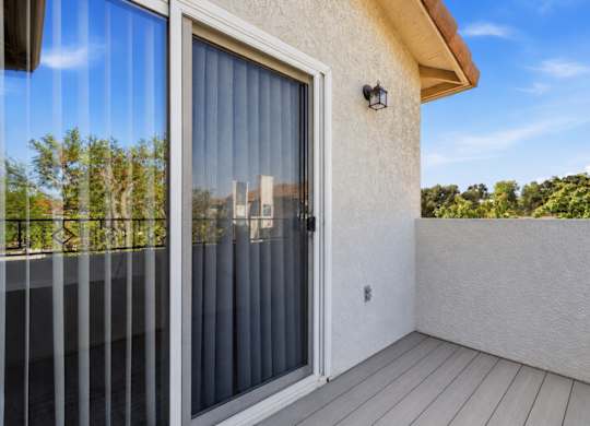 A balcony with a glass door and a white wall.
