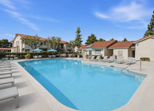 A resort style swimming pool with lounge chairs and umbrellas.