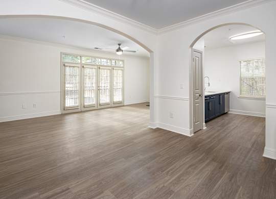 an empty living room and kitchen with wood flooring and white walls