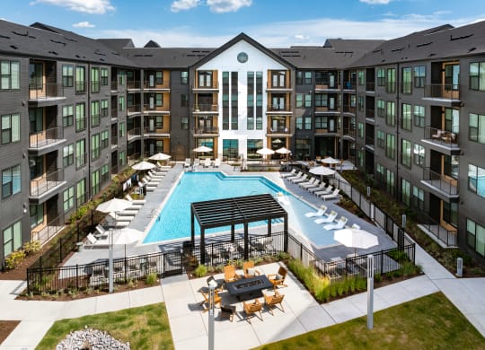 an outdoor pool with lounge chairs and tables in front of an apartment building