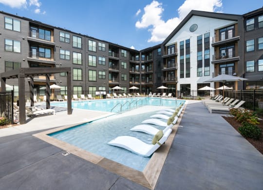 a swimming pool with white lounge chairs in front of an apartment building