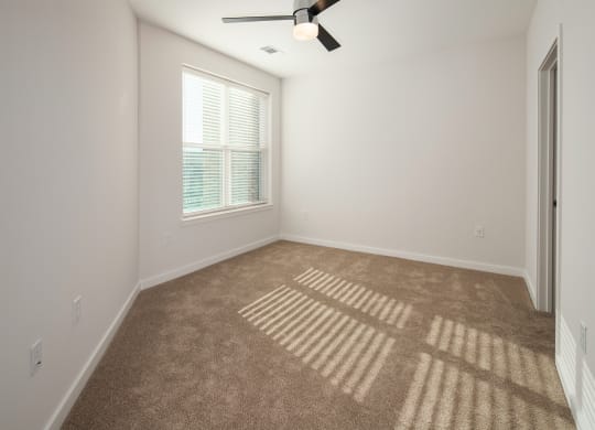 an empty living room with a window and a ceiling fan