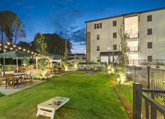 a grassy yard with tables and chairs and buildings with lights