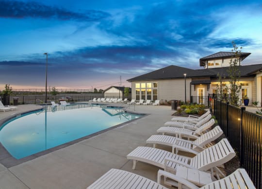 a pool with white chairs and a building with a blue sky