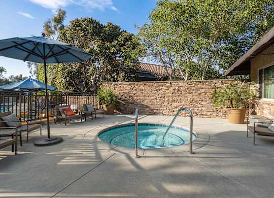 A pool with a blue umbrella and a stone wall.
