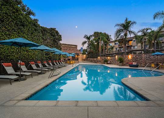 A pool surrounded by lounge chairs and umbrellas at dusk.