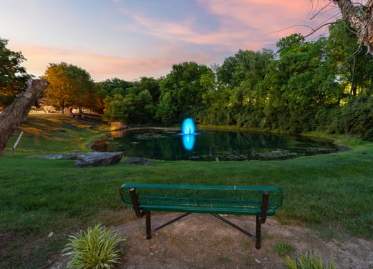 a bench in front of a pond with a blue fountain