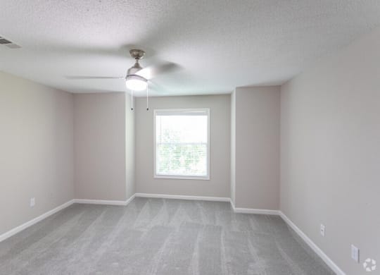 an empty living room with a ceiling fan and a window
