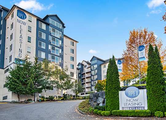 an apartment building with a sign for now leasing in front of a road