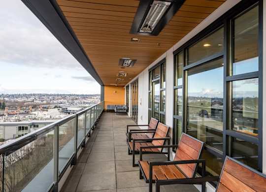 A balcony with wooden benches and glass railings overlooking a cityscape.at Axle, Seattle, 98119 