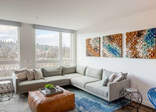 A living room with a grey couch, a brown leather ottoman, and three abstract paintings on the wall.at Axle, Washington, 98119