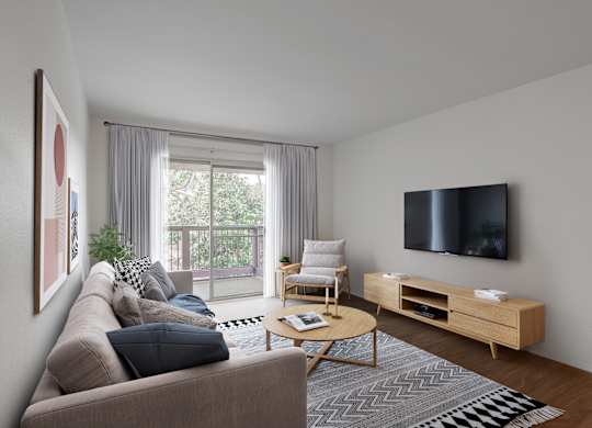 A living room with a grey couch, a wooden coffee table, a flat screen TV, and a large window with curtains.