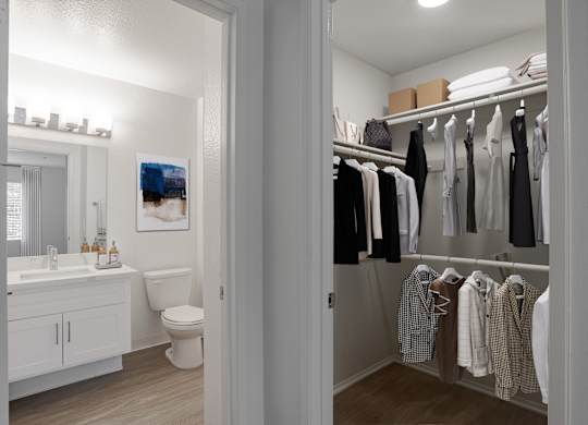 A white bathroom with a toilet, sink, and a closet with clothes.