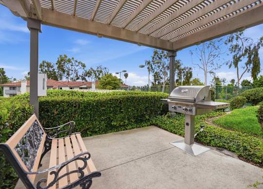 A picnic table with a grill and a bench under a canopy.
