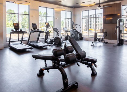 a workout room with weights and chairs in a large room with windows