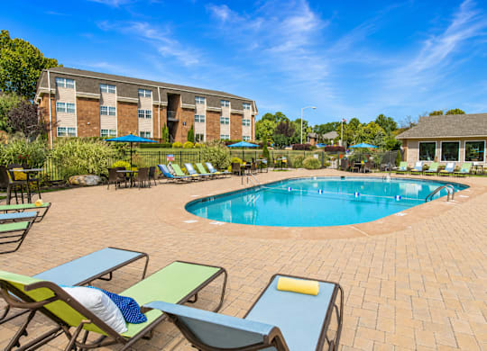 A pool surrounded by chairs and umbrellas with a building in the background.