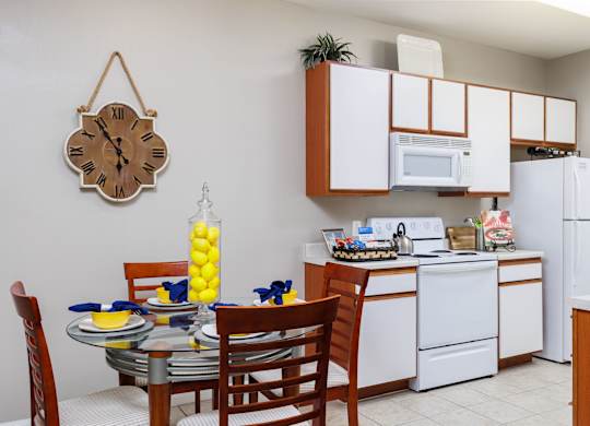 A kitchen with a table set for two and a clock hanging on the wall at Clear Creek Meadows Apartments, Copperas Cove, TX, 76522