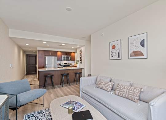a living room with a couch a chair a table and a kitchen in the background