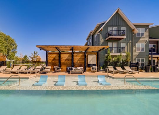 a swimming pool with blue chairs in front of a house