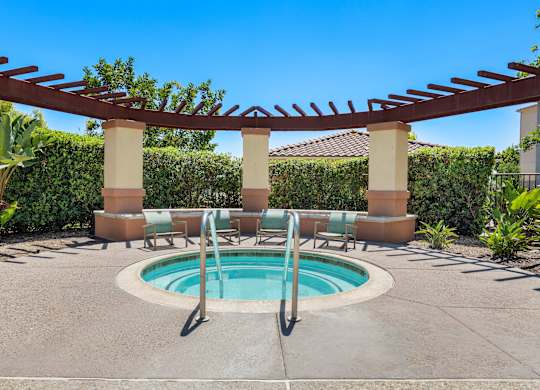 A pool surrounded by a concrete patio and a pergola.