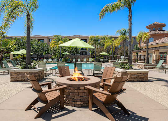 A fire pit surrounded by chairs in a sunny outdoor setting.