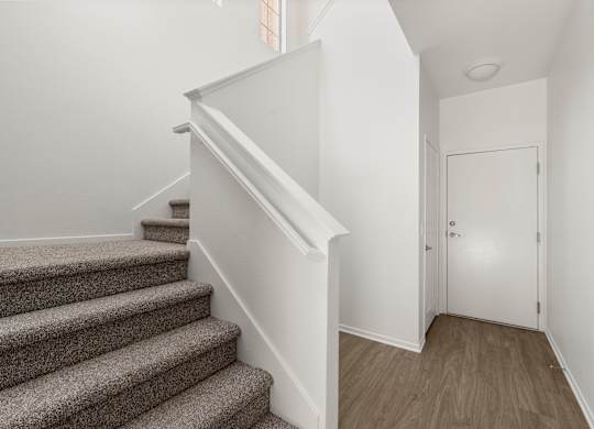 A staircase with a carpeted runner and wooden steps leads up to a white door.