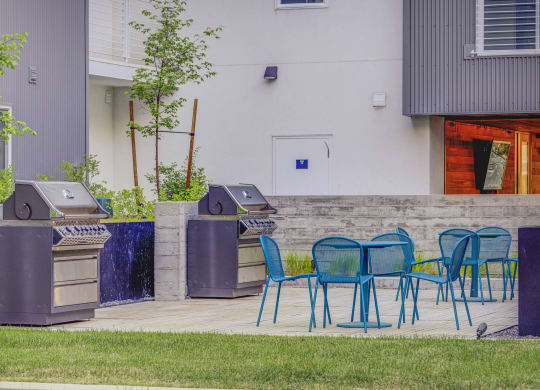 two bbq grills and blue chairs on a patio in front of a building