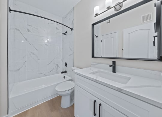 a bathroom with white cabinets and a white toilet next to a white bathtub with a shower