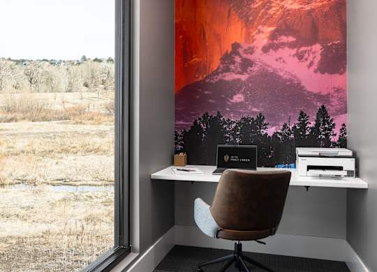 A room with a chair and a desk with a laptop and a printer on it.