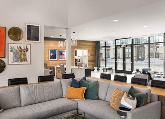 A grey couch with multiple pillows sits in the middle of a room with a wooden table and chairs.