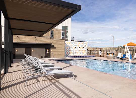 A pool with chairs and a building in the background.