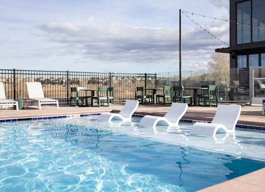 A pool with white chairs and a building in the background.