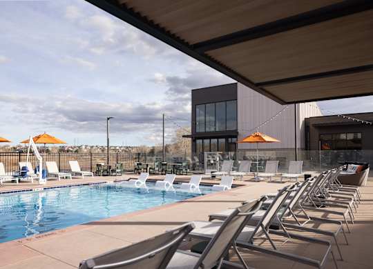 A pool with chairs and umbrellas in front of a building.