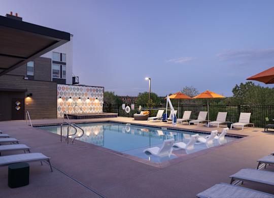 A pool with lounge chairs and umbrellas is surrounded by a building.