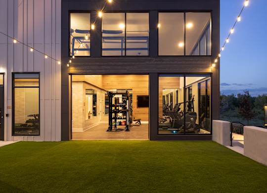 A modern house with a glass wall and a green lawn in front.