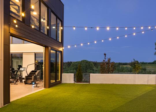 A modern house with a glass wall and a green lawn.