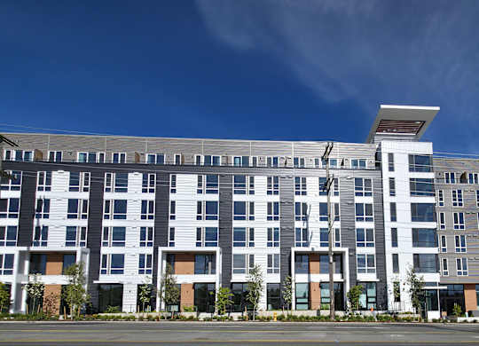 A large, modern multi-story building with a flat roof and a mix of white and dark grey balconies.