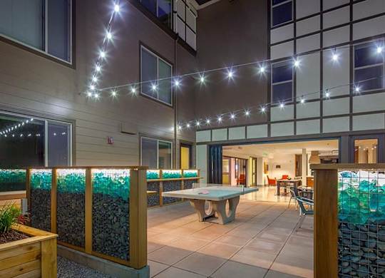 Outdoor courtyard with decorative glass wall panels and string lights at Six Oaks Apartments, Washington, 98011