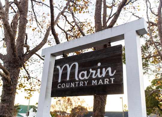 A sign for Marin Country Mart is displayed on a tree.