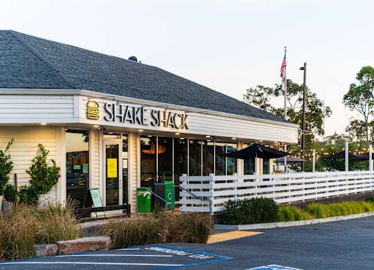 A Shake Shack restaurant with a white picket fence in front.