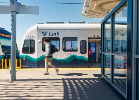 a man walking on a platform in front of a white and blue train at Ion Town Center, Shoreline Washington