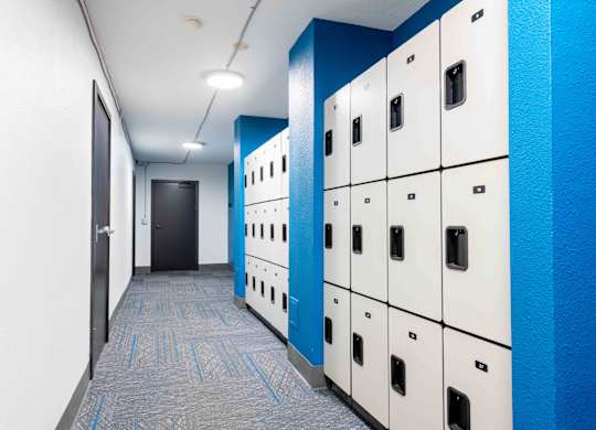 A hallway with a row of lockers on the right and a door on the left.