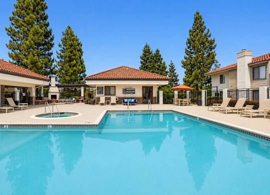 A large swimming pool in front of a house with a patio and trees in the background.