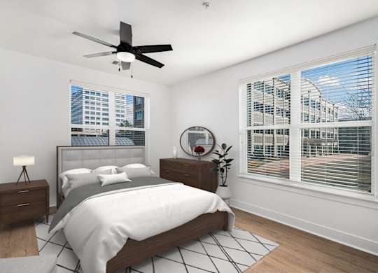 A bedroom with a large bed, a ceiling fan, and a view of a cityscape through the window.