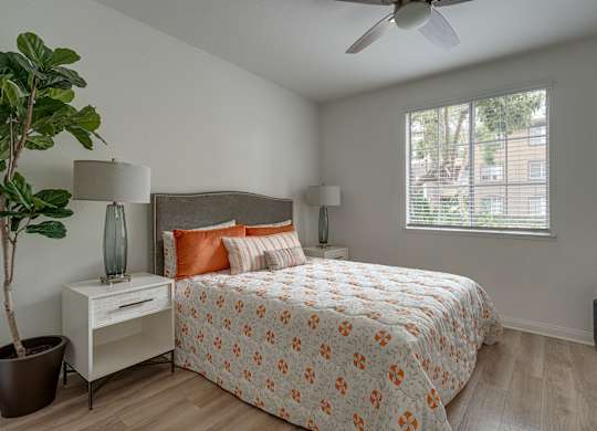 A bedroom with a bed, nightstand, and a plant.