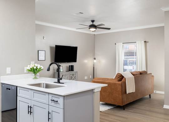 A kitchen with a sink, a fridge, a microwave, a counter, a fan, a sofa, a window, and a vase of flowers at Clear Creek Meadows Apartments, Copperas Cove, Texas