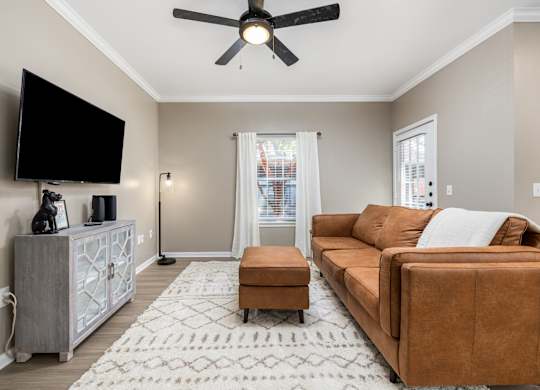 A living room with a brown couch, a television, and a ceiling fan at Clear Creek Meadows Apartments, Texas, 76522